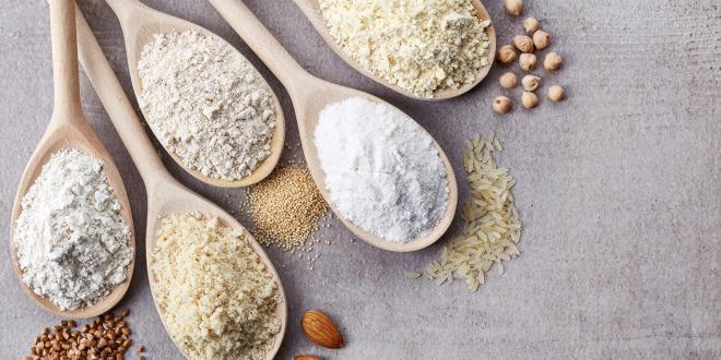 Wooden spoons of various gluten free flour on a light gray background.