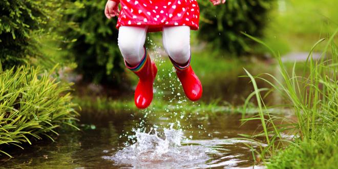 Young girl with red rubber boots jumping up from a creek.