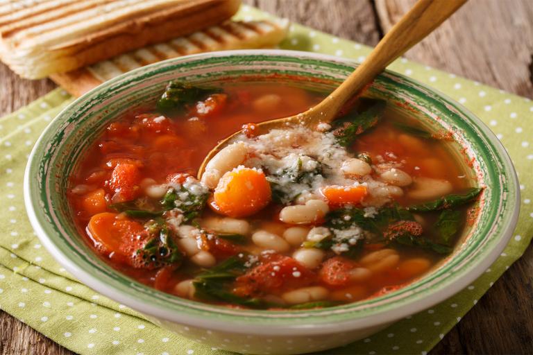 a bowl of tomato-based soup with beans and spinach